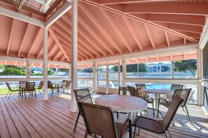 Een overdekt terras met tafels en stoelen, een zwembad op de achtergrond en uitzicht op een woonwijk.