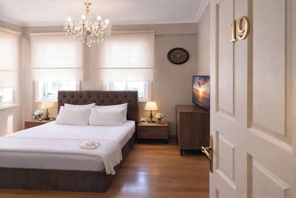 Una habitación de hotel con una cama grande, una araña, un reloj y un televisor sobre un mueble de madera.
