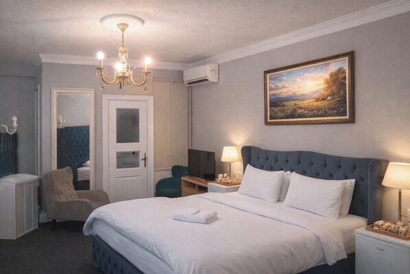 Una habitación de hotel con una cama grande, un televisor, un escritorio con una lámpara y un cuadro en la pared.