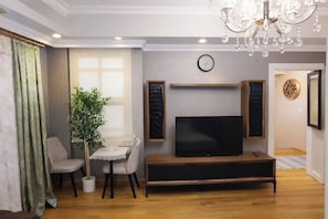 A living room with a flat-screen TV, a wooden entertainment unit, a potted plant, a dining table with chairs, and a chandelier. - Charming Double Room with AC in Vibrant Istanbul (istanbul)