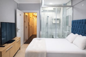 A hotel room with a bed, a television, a wardrobe, and a glass-enclosed shower area. - Charming Double Room with AC in Vibrant Istanbul (istanbul)