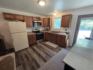 A kitchen with wooden cabinets, a stainless steel refrigerator, a microwave, an oven, and a sink. - Cozy 1-bedroom apartment in enchanting Sparta surounded by trees and wilderness. (Sparta)
