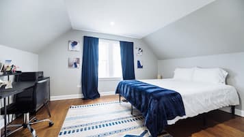 A bedroom with a bed, desk, chair, and a window with curtains.
