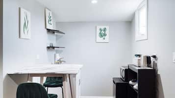 Una cucina compatta con un piano di lavoro bianco, una sedia verde e un elettrodomestico nero.