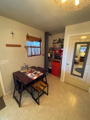 Un espacio habitable compacto con una mesa de comedor, un refrigerador rojo y una ventana con cortinas.
