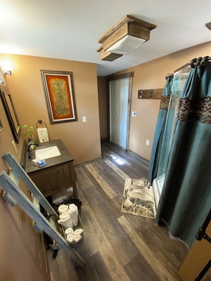 Un baño con tocador de madera, lavamanos, toallero y cortina de ducha.