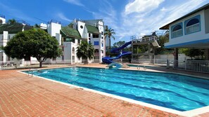 A swimming pool with a water slide, surrounded by buildings with balconies and palm trees. - New Listing (El Rodadero)