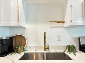 Une cuisine moderne dotée d’appareils électroménagers en acier inoxydable, d’un robinet doré et de meubles blancs.