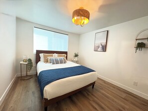 Une chambre à coucher comprenant un lit, des tables de chevet, une fenêtre, une plante fixée au mur et un luminaire au plafond.