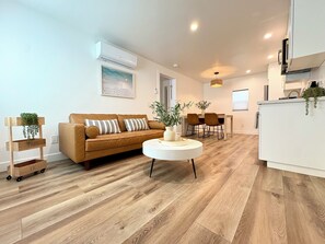 A modern living room with a brown sofa, a white coffee table, and a dining area with chairs. - 3766 Beautiful North Park Getaway-Close to Everything (San Diego)