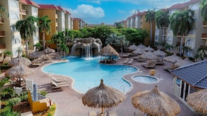 Un resort con una piscina central, varias zonas de descanso con sombrillas y una cascada.