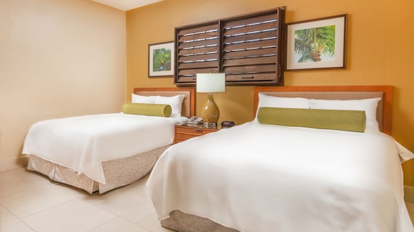 Habitación de hotel con dos camas, una mesita de noche, una lámpara y dos cuadros en la pared.