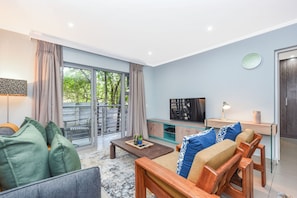 Ein modernes Wohnzimmer mit Sofa, Couchtisch, Fernseher und einem Balkon mit Vorhängen.