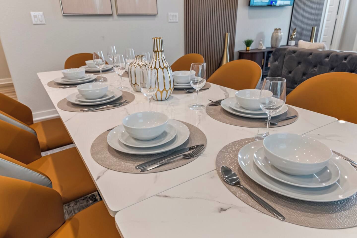 Een eettafel gedekt met witte borden, kommen en bestek, omringd door oranje stoelen.