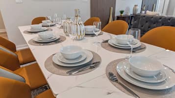 Een eettafel gedekt met witte borden, kommen en bestek, omringd door oranje stoelen.