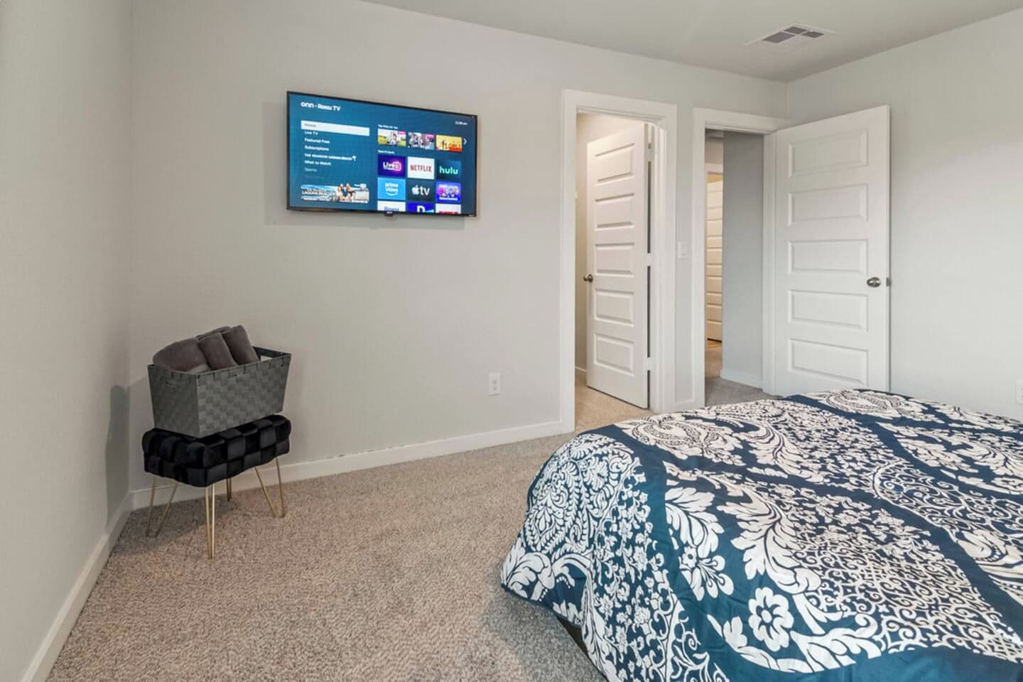Een slaapkamer met een bed, een aan de muur bevestigde televisie waarop streamingdiensten worden weergegeven, een deur en een zithoek met kussens.