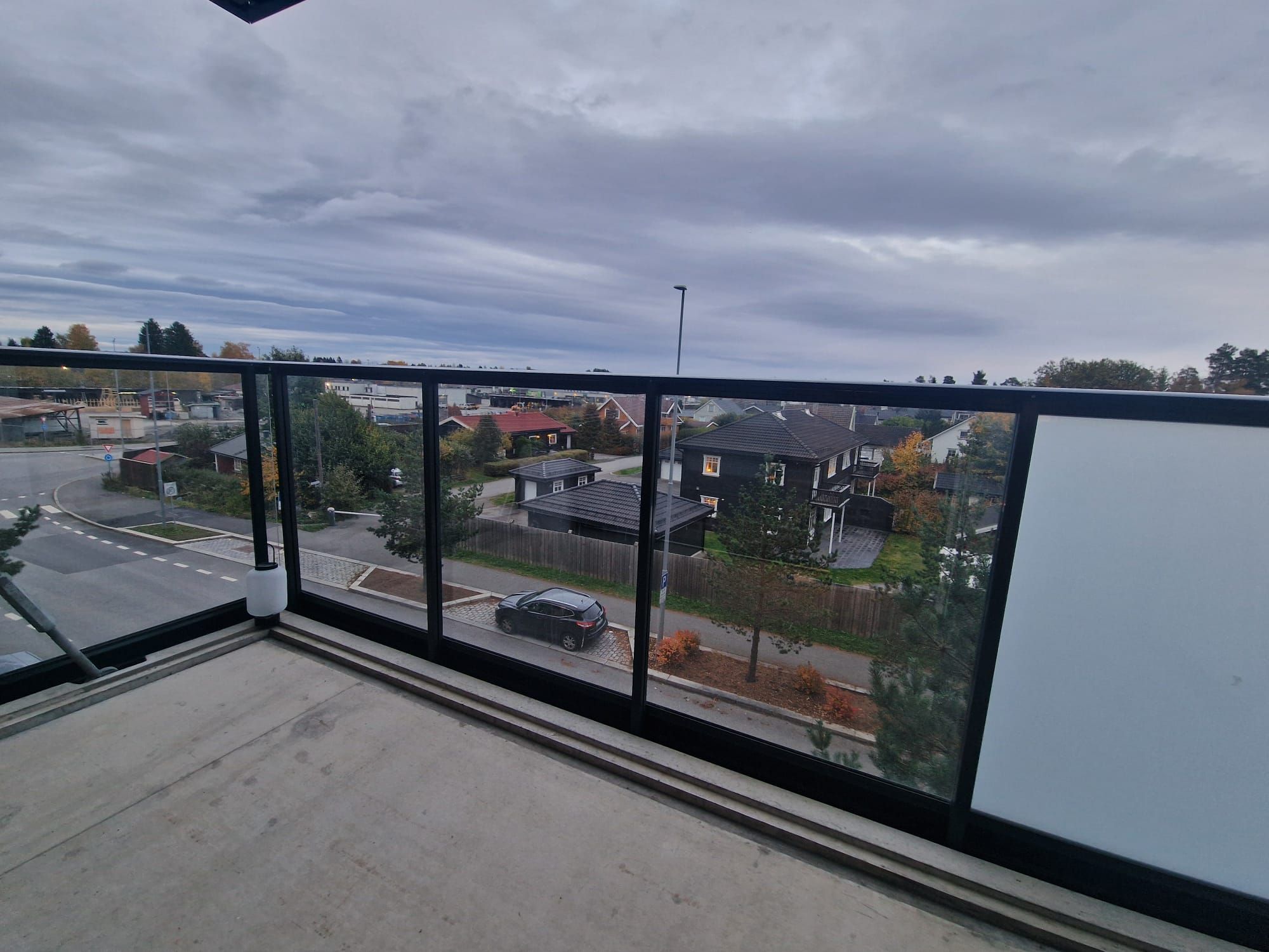 En balkon med udsigt over en vej med huse og en bil.