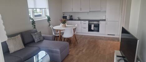 A compact living space with a sofa, a small round table, a kitchenette, and a TV.