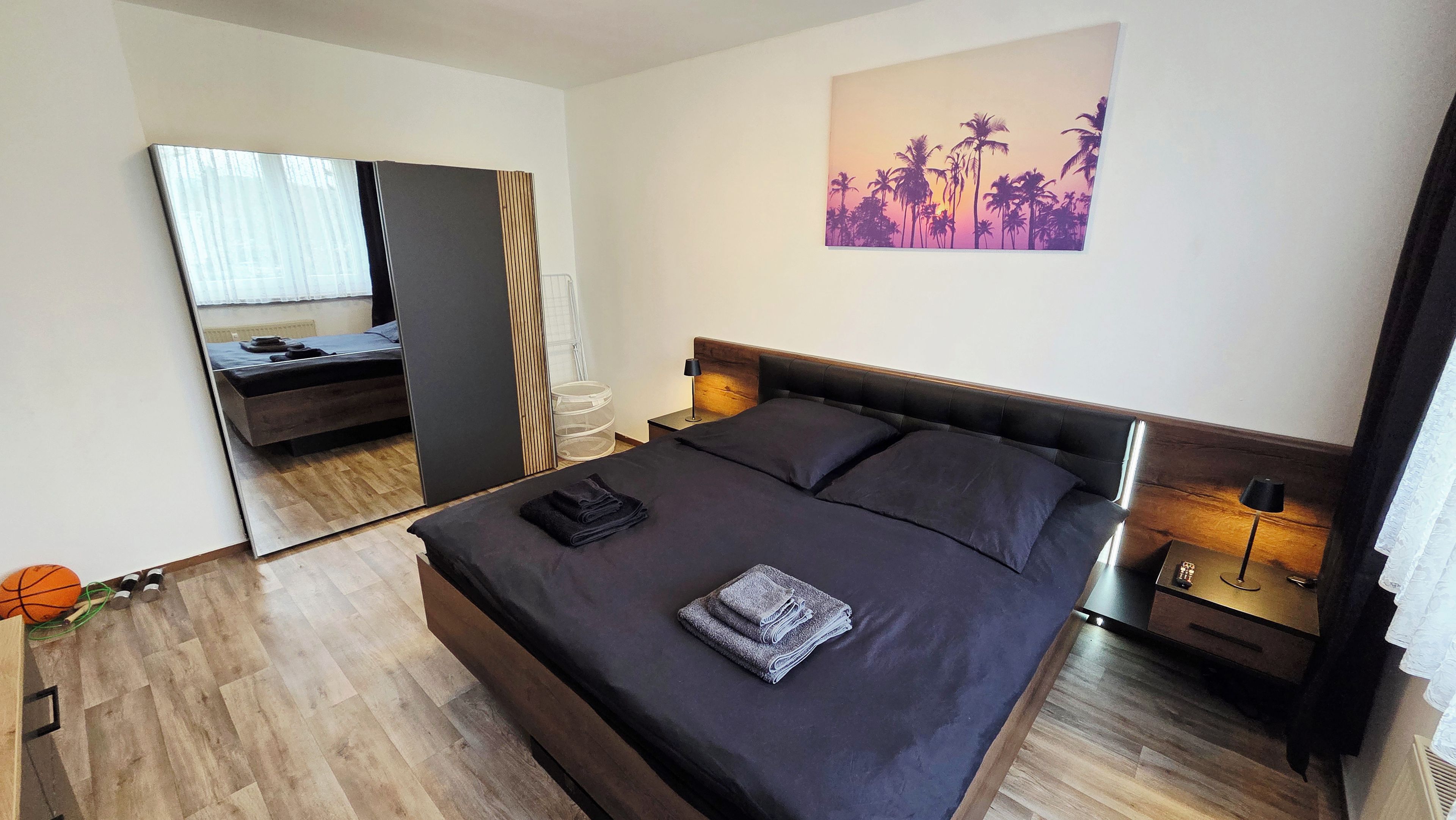 A modern bedroom with a large bed, a bedside table, a nightstand, a mirror, and a wall art piece.