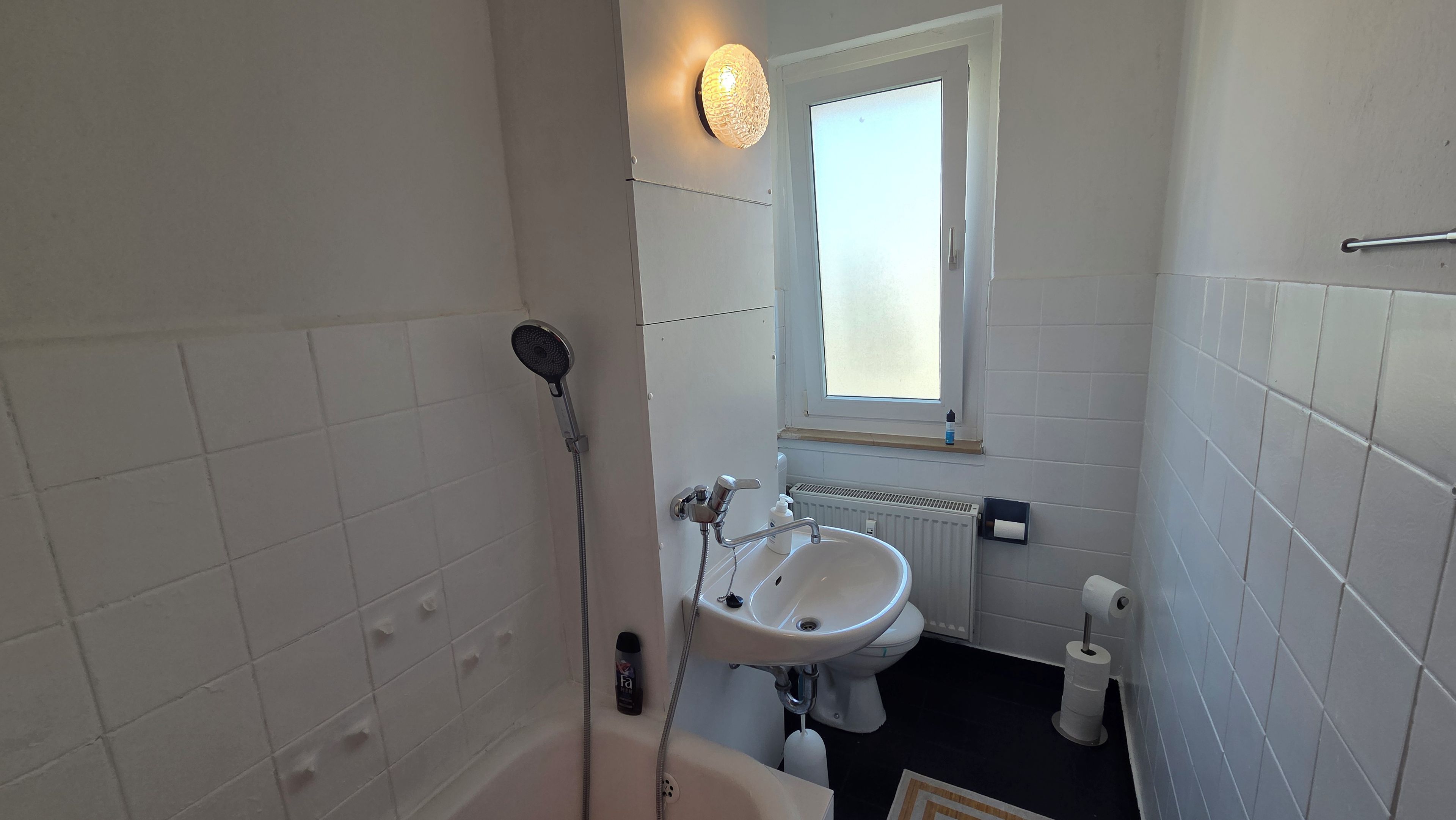 A bathroom with a shower, sink, toilet, and a window.