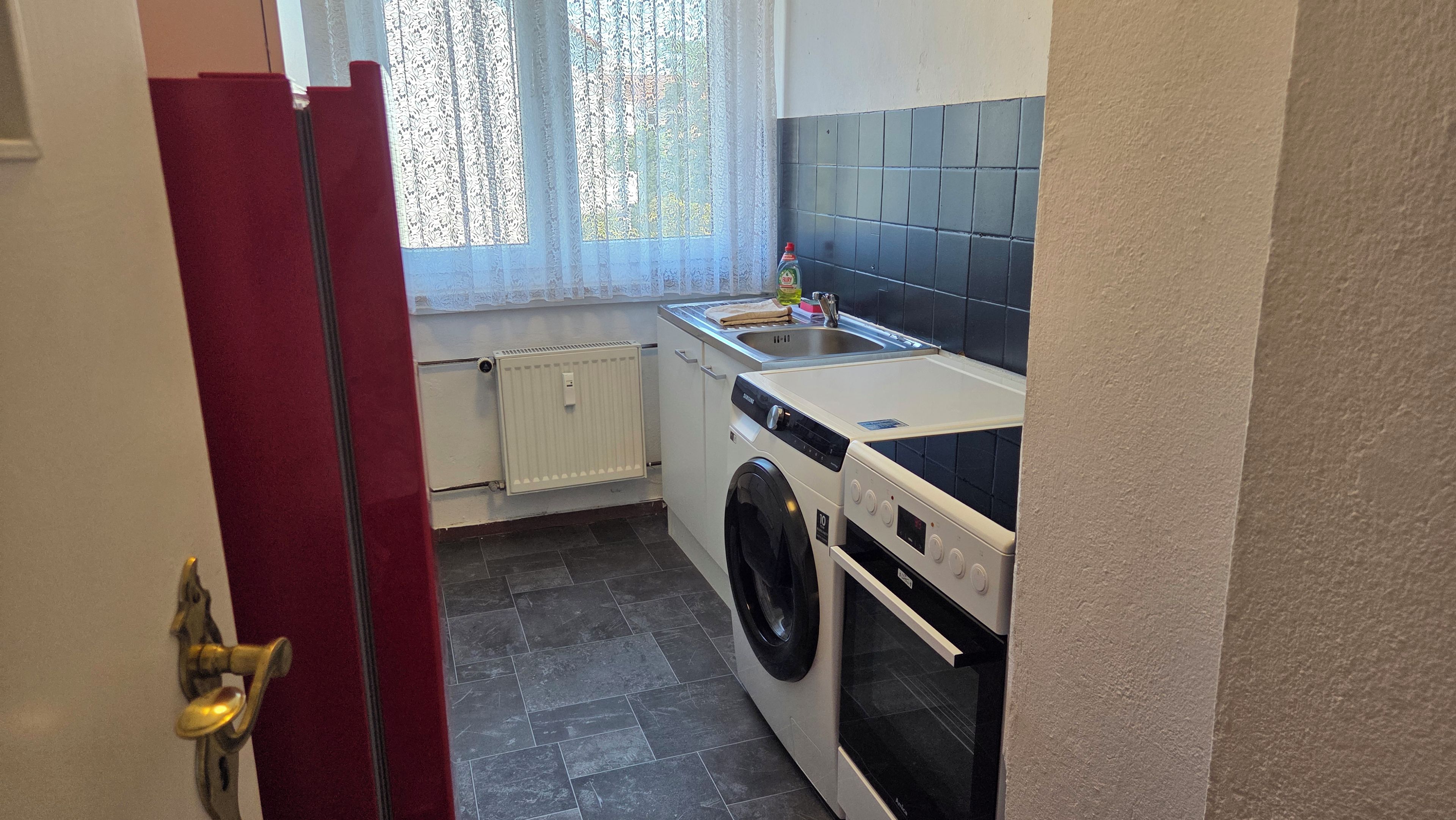 A compact kitchen with a washing machine, a sink, and a tiled backsplash.