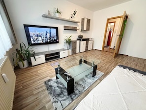 Ein modernes Wohnzimmer mit Flachbildfernseher, Glastisch, Holzboden und weißem Teppich.