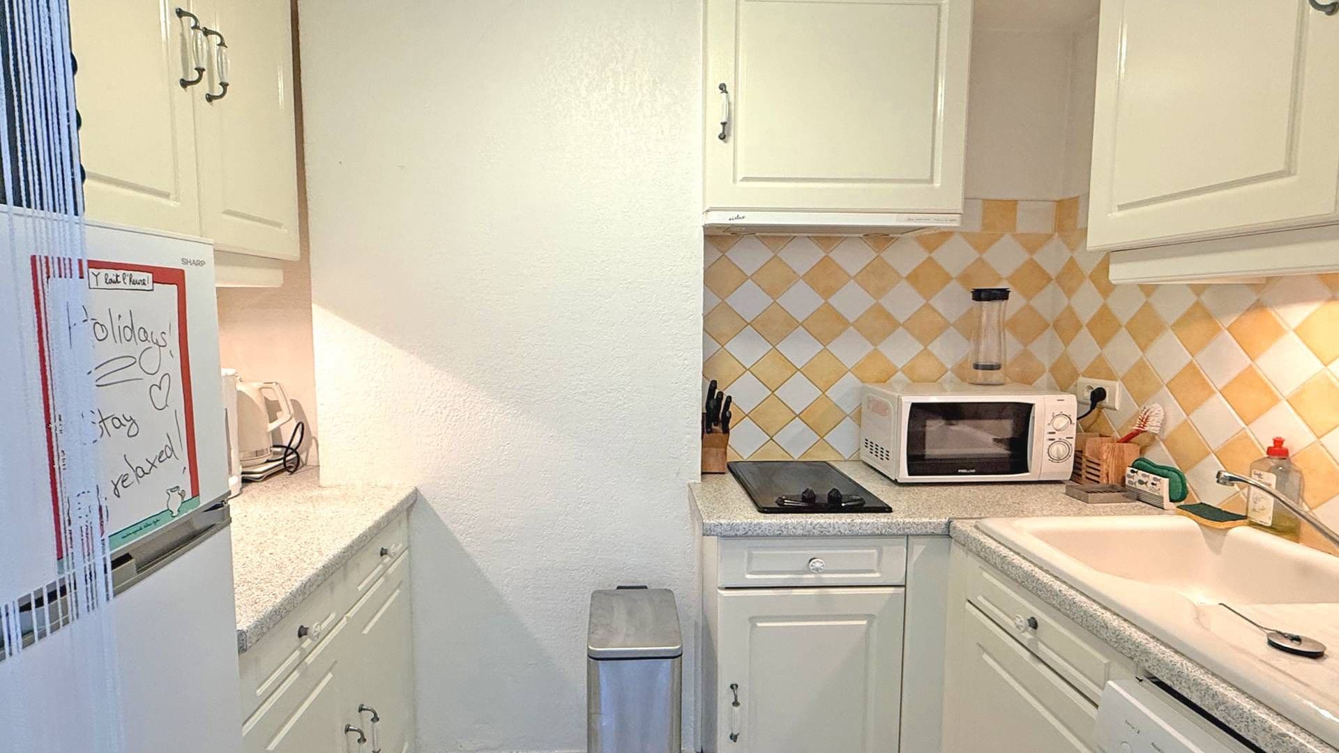 A compact kitchen with white cabinets, a microwave, and a small trash bin.