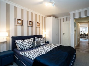 A bedroom with a bed, bedside tables, a wardrobe, and a door leading to a bathroom. - Holiday Apartment With 1 Bedroom (Sylt)