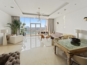 A spacious living room with a large glass door leading to a balcony, a dining table with chairs, and a sofa. - Tiara Aquamarine - 705 3BD (Dubai)