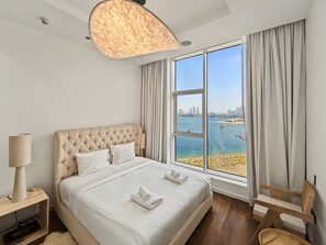 A hotel room with a large bed, a view of the sea, and a cityscape. - Tiara Aquamarine - 705 3BD (Dubai)