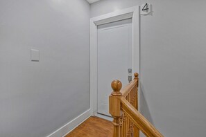 A hallway with a white door, a wooden staircase railing, and a light switch on the wall. - Walk to Metro - 1.2 Miles to NIH & Walter Reed (Bethesda)