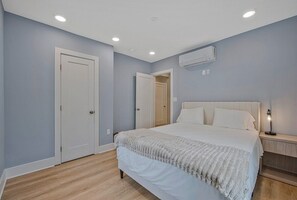 A bedroom with a bed, a nightstand, an air conditioning unit, and a door. - Walk to Metro - 1.2 Miles to NIH & Walter Reed (Bethesda)