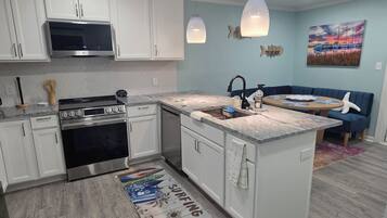 Una cocina moderna con gabinetes blancos, estufa de acero inoxidable y encimera de granito.
