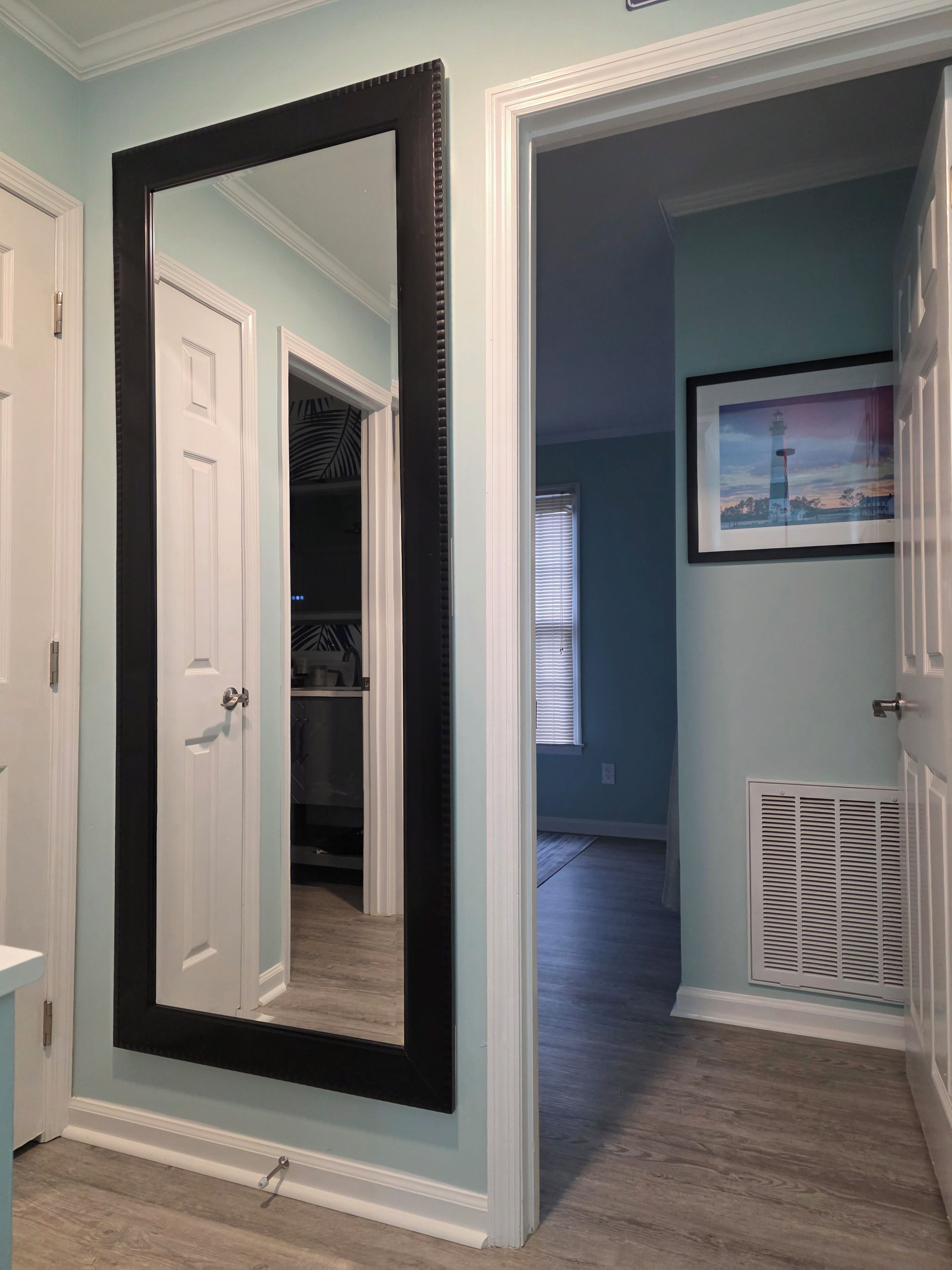 A hallway with a large mirror, a door, a closet, and a vent.