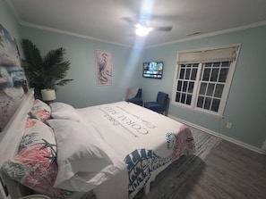 A bedroom with a bed, a ceiling fan, a TV, a window, and a plant. - 2-bedroom condo in enchanting Morehead City minutes away from Atlantic Beach (Morehead City)