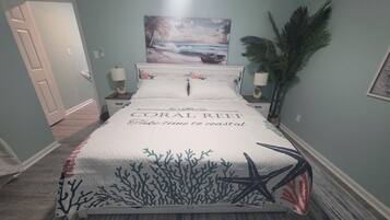 A bedroom with a bed featuring a coral reef design, a painting of a beach scene, and a potted plant.