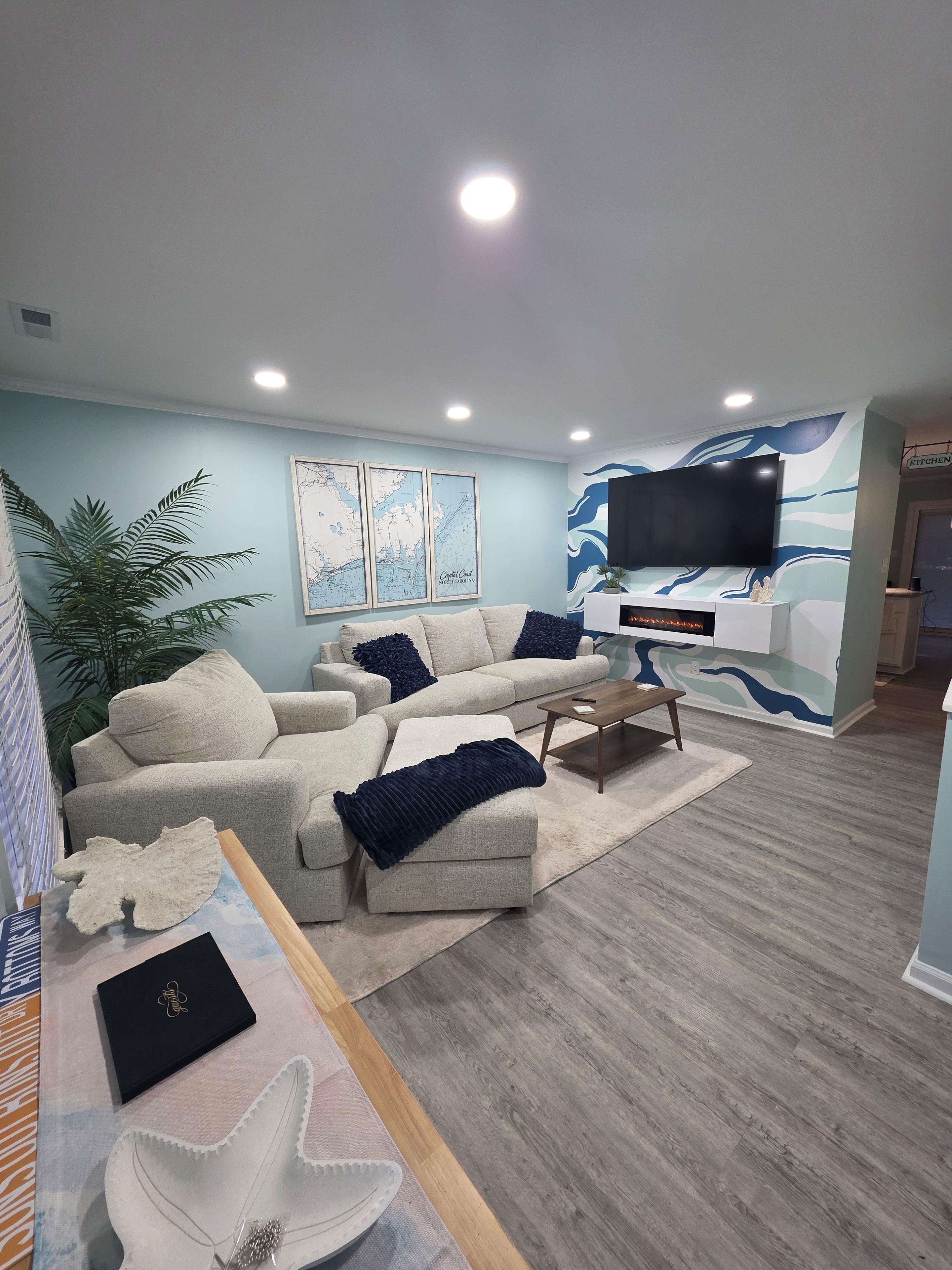 Een moderne woonkamer met een hoekbank, een flatscreen televisie en een decoratieve wand met een golfpatroon.