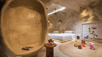 A bedroom with a large, curved wall, a bed, a small table, and a play area with toys.
