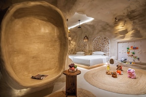 A bedroom with a large, curved wall, a bed, a small table, and a play area with toys.