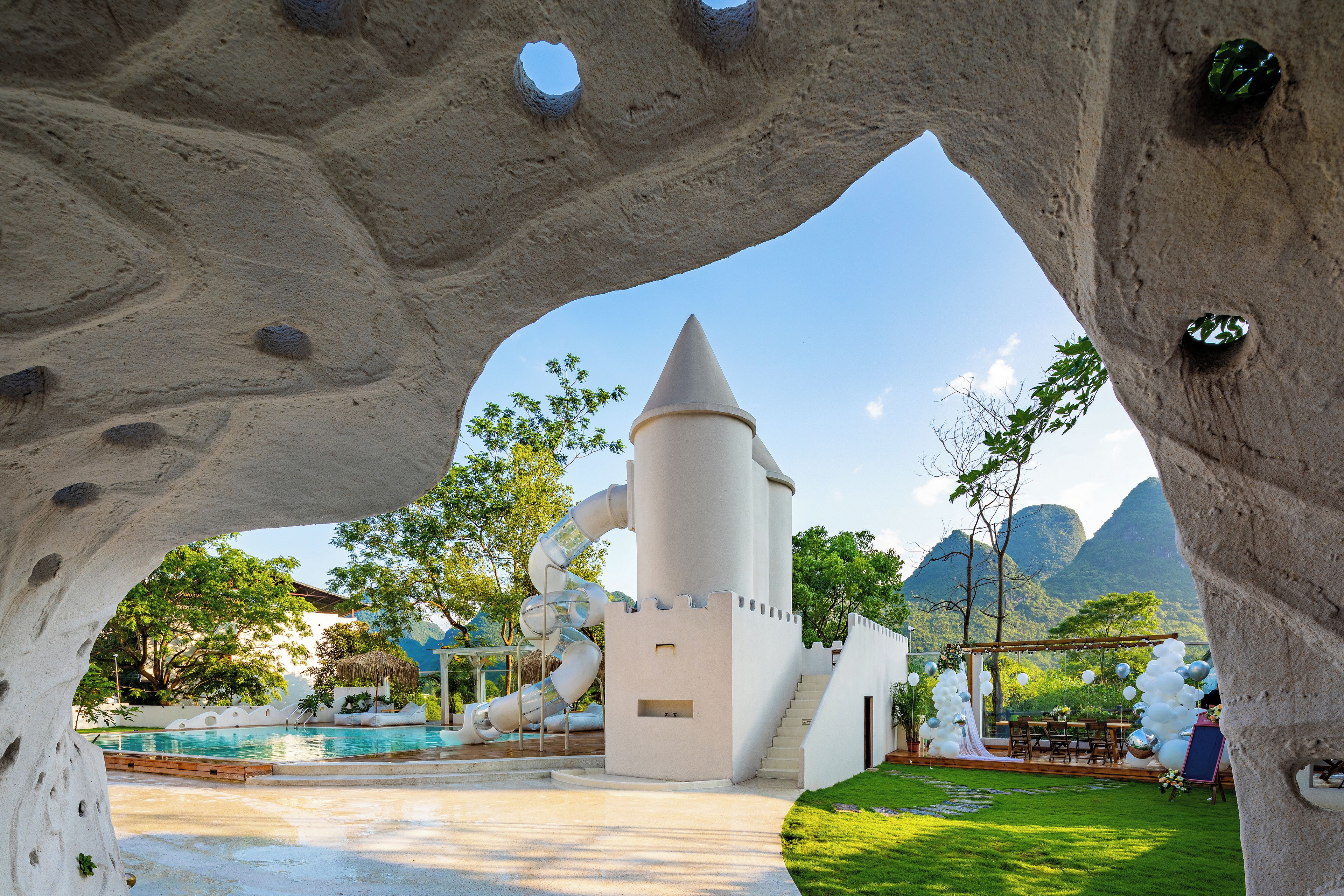 A unique architectural structure with a conical tower and a slide, surrounded by a pool and greenery.