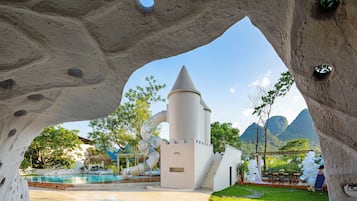 A unique architectural structure with a conical tower and a slide, surrounded by a pool and greenery.