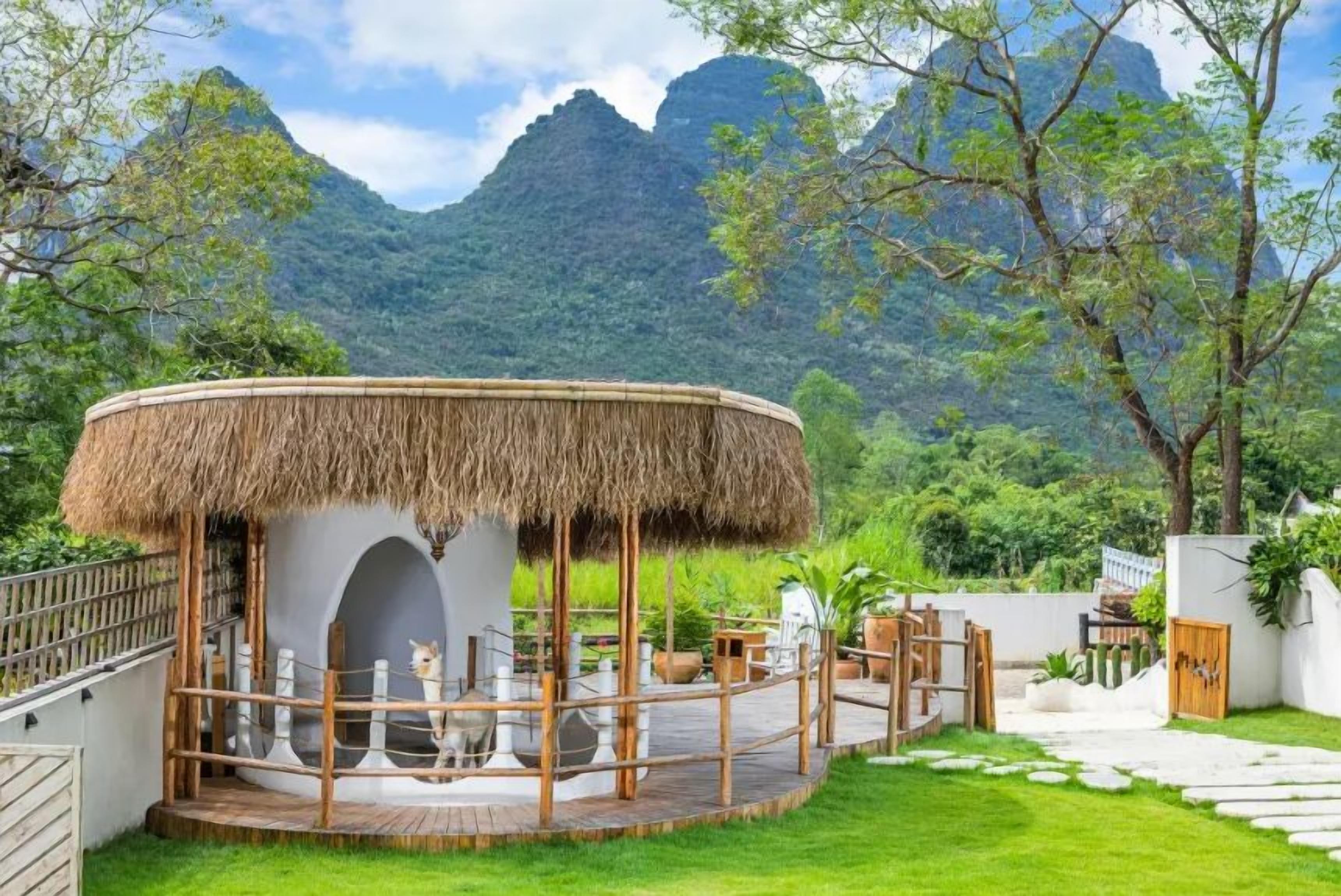 A circular structure with a thatched roof, surrounded by a wooden deck and a white wall.