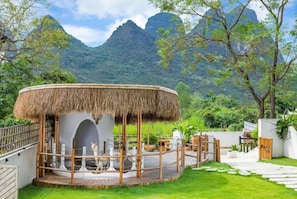 A circular structure with a thatched roof, surrounded by a wooden deck and a white wall. - Yangshuo OrangeWhite Resort - An Exclusive Cave - Inspired Haven by Yulong River (Guilin)