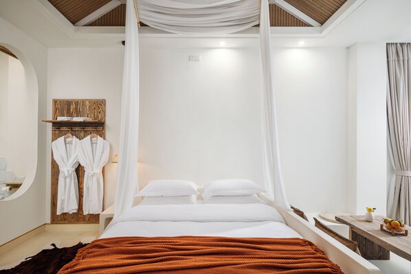 A bedroom with a large bed, white bedding, a wooden headboard, a bedside table with a vase, and a cowhide rug.