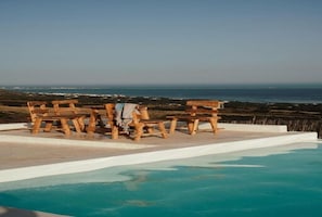 Una piscina amb seients de fusta i vista a l'oceà.