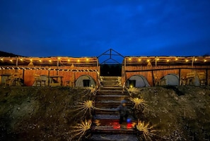 A building with a staircase leading to a covered entrance, surrounded by walls adorned with string lights. - Outdoor Tent 5 (Ghar meleh)