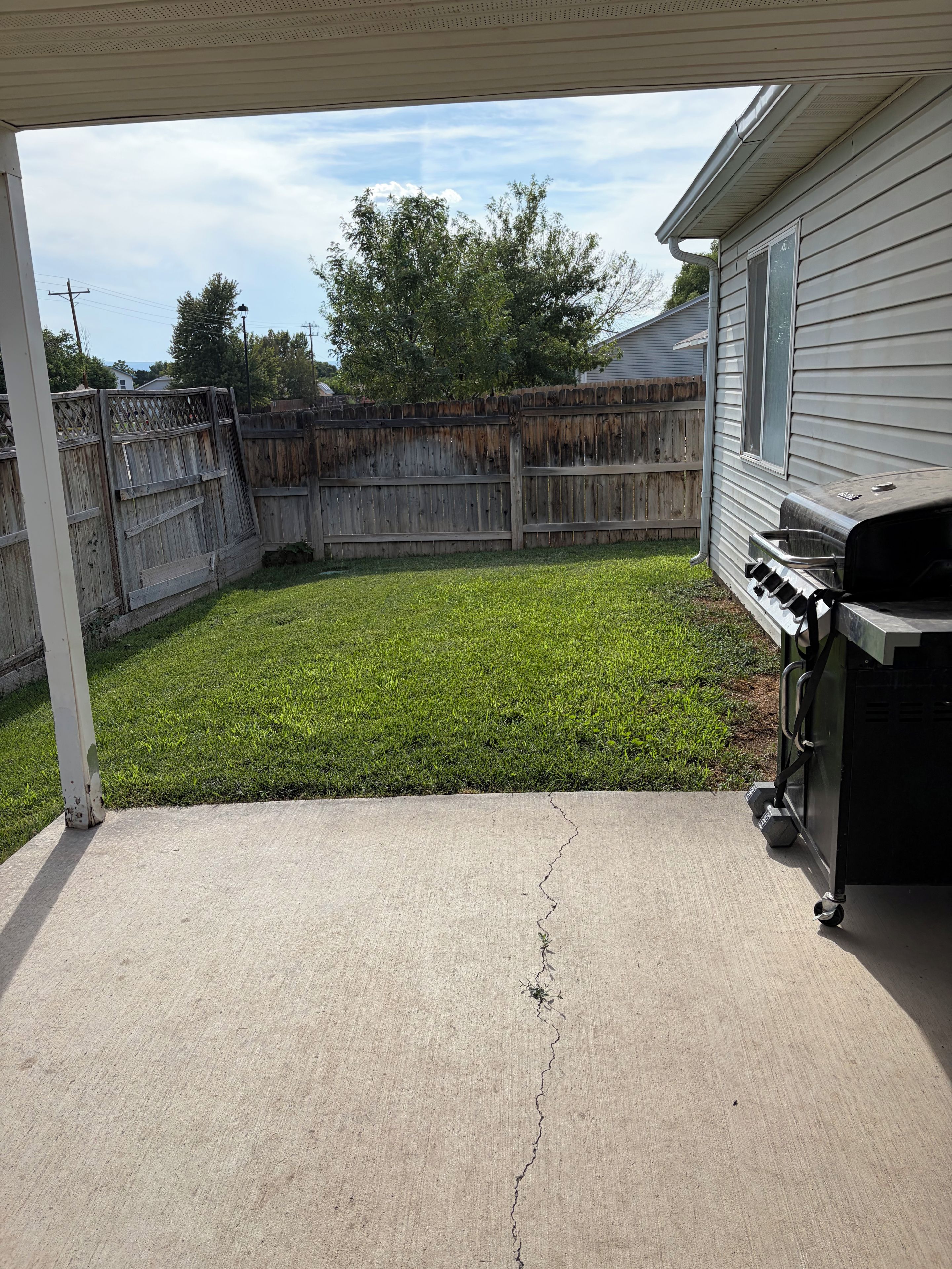 A backyard with a concrete patio, a wooden fence, and a barbecue grill.