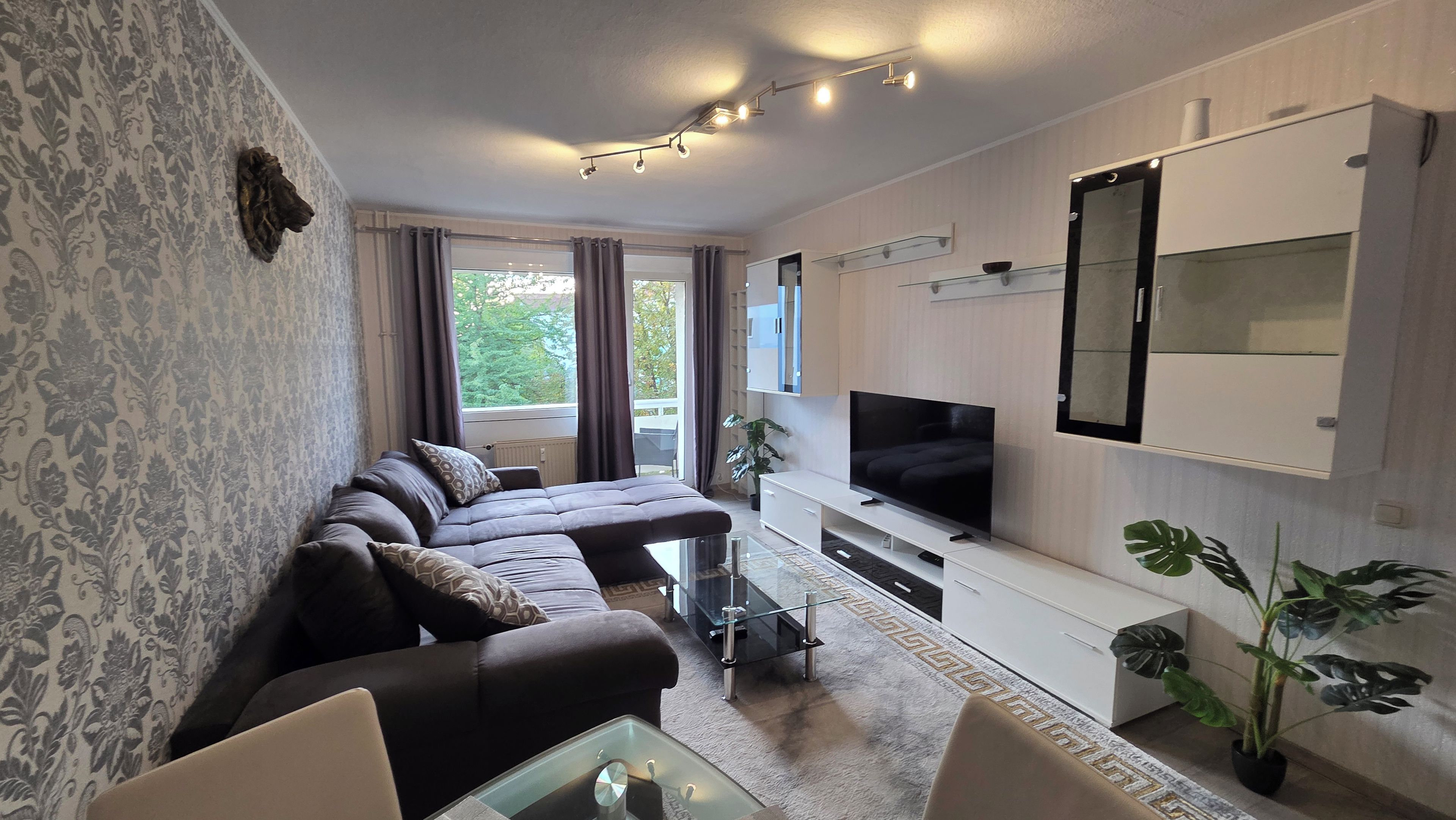 A modern living room with a sectional sofa, a flat-screen TV, and a glass coffee table.