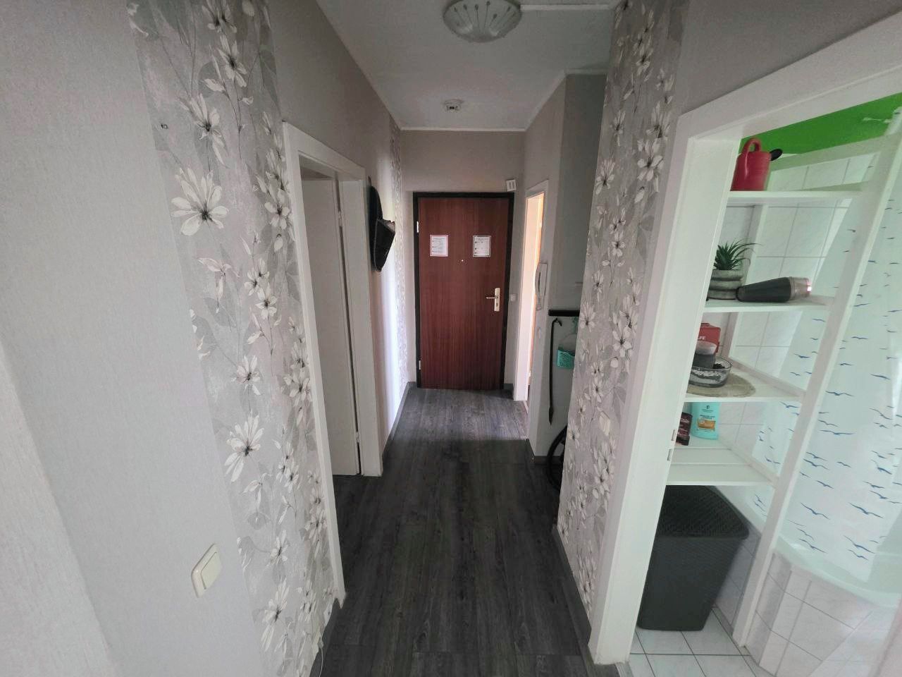 Un pasillo con una puerta de madera al final, un estante con diversos objetos y una pared con diseño.