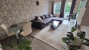 Un salon moderne avec une table à manger en verre, un canapé foncé et un tapis à motifs.